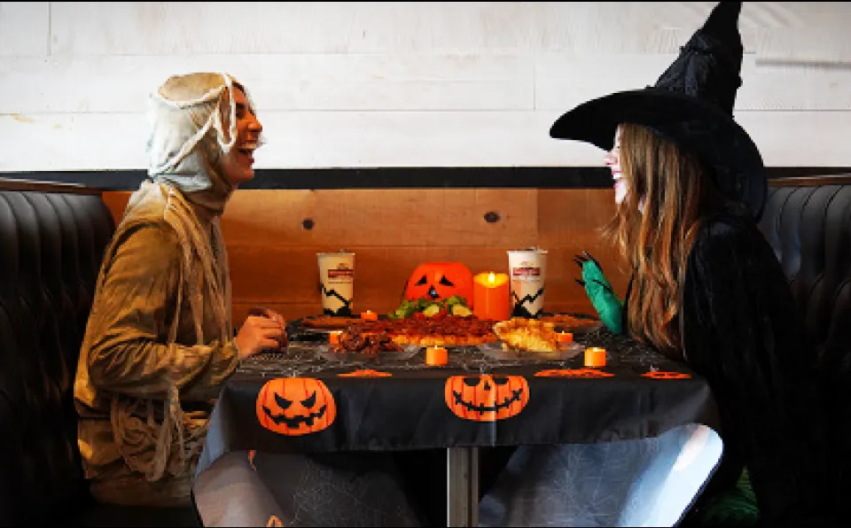 Two guests dressed as a mummy and a witch sharing pizza at a Mountain Mike's booth