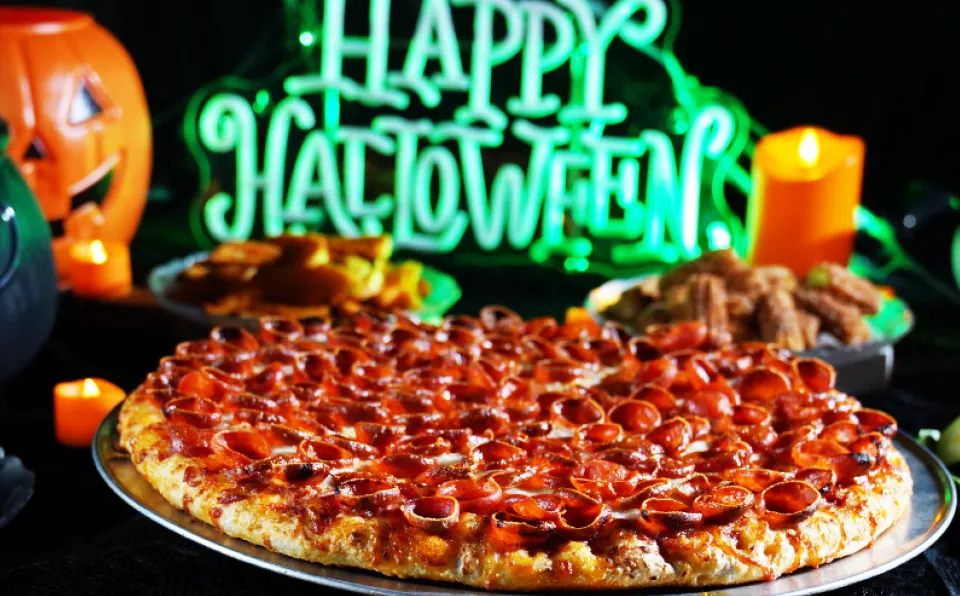 A pepperoni pizza under a neon Happy Halloween sign